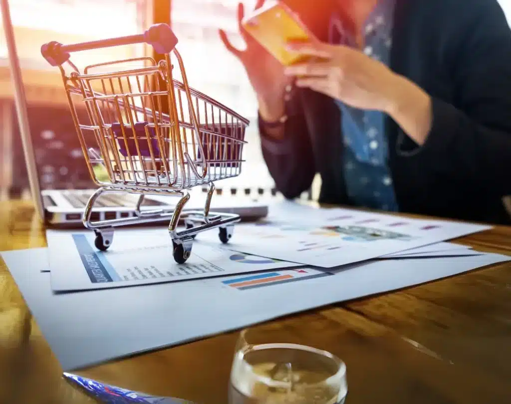 Mini carrinho de compras sobre documentos de negócios com gráficos, simbolizando vendas e gestão integrada.